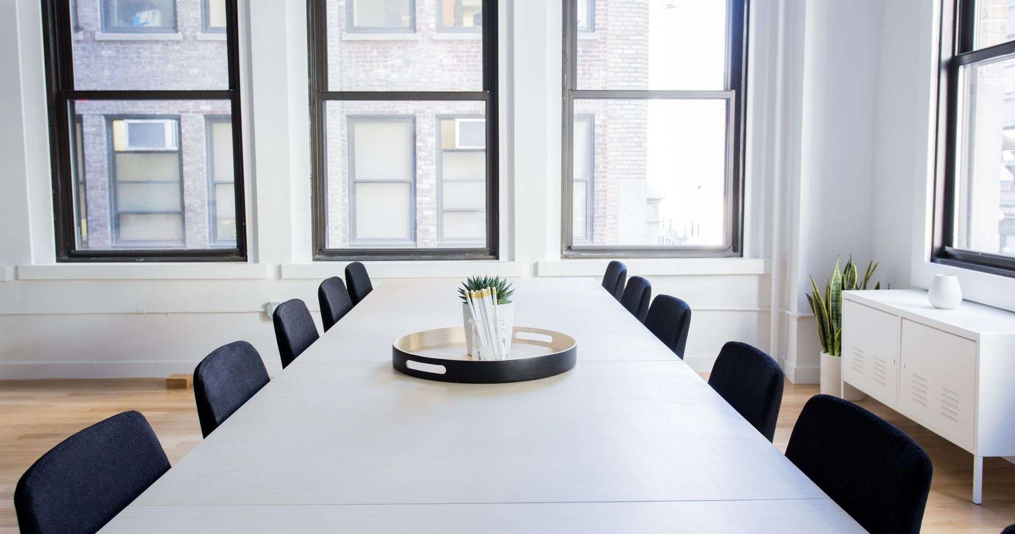 Sala de reuniones vacía con una mesa larga blanca, sillas negras y ventanales