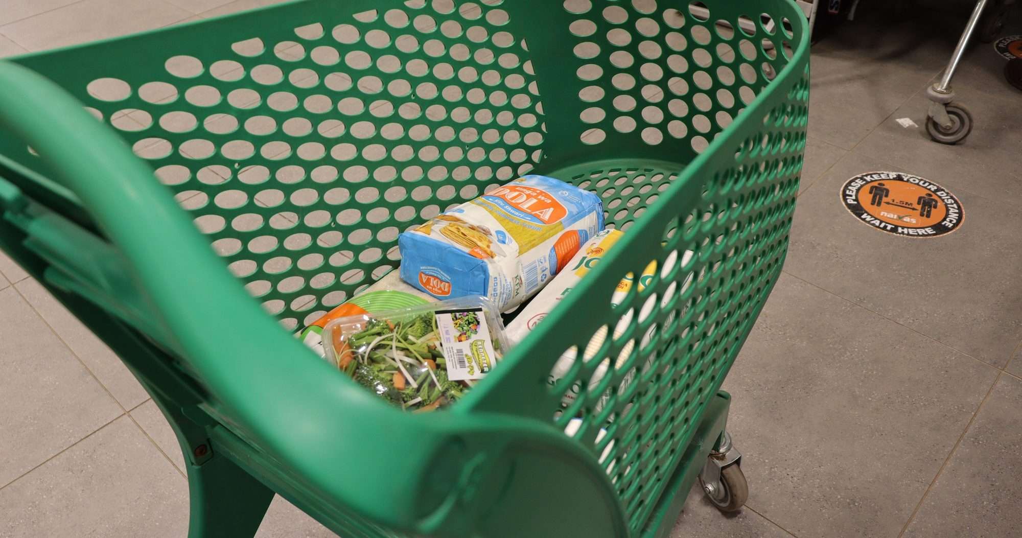 Carro de la compra verde con harina, verduras y otros productos en el pasillo de un supermercado